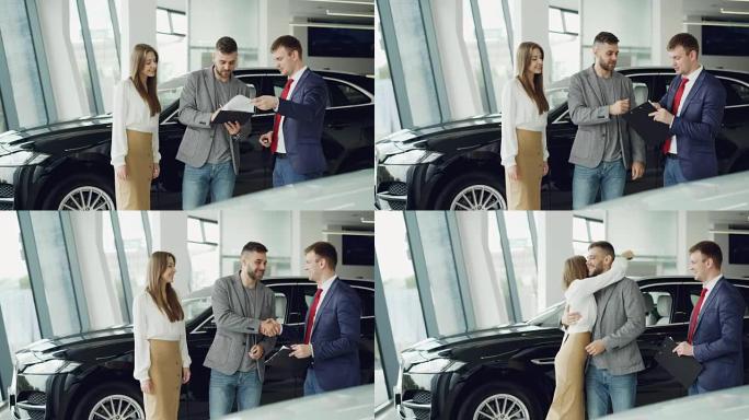 年轻的大胡子男人正在为他迷人的妻子买车，他签署了与经理握手的文件，并获得了密钥卡，然后将其交给女人，