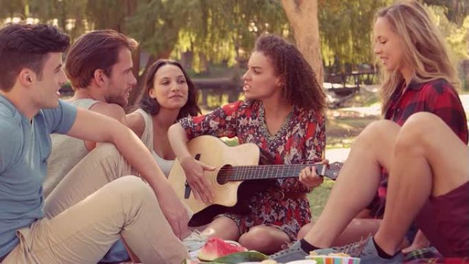 时髦的女人和她的朋友在公园弹吉他