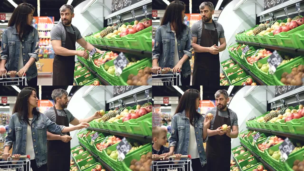 有吸引力的女人感兴趣的顾客正在与在超市水果部门工作的帅哥友好推销员交谈，女人正在闻新鲜水果。