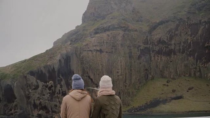 两个时尚女人在岛上行走的背景图。游客望向绿山，探索冰岛