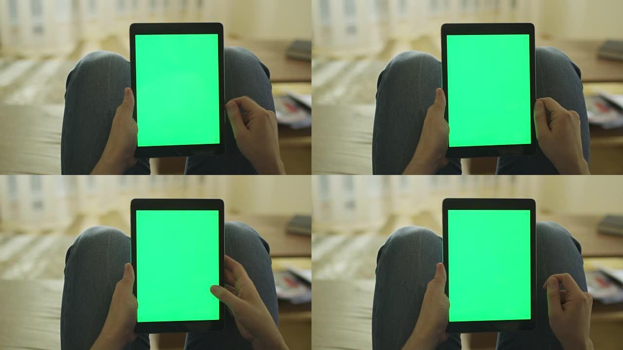 男子躺在家里的沙发上，在膝上的纵向模式下使用带有绿屏的平板电脑
