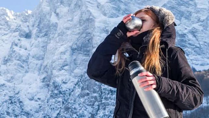 年轻女子在冬季景观中从热水瓶中喝水