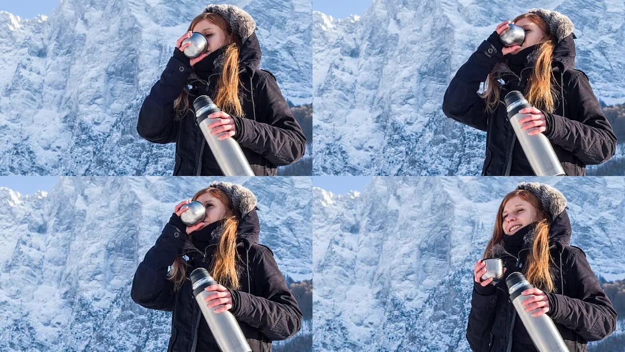 年轻女子在冬季景观中从热水瓶中喝水