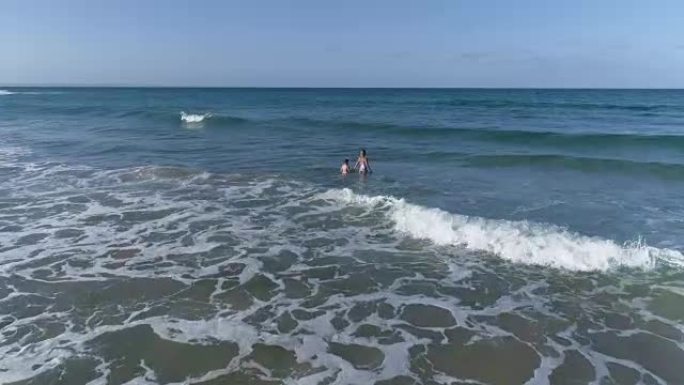 在海中浅浪中游泳的年轻女子和年轻男孩的鸟瞰图