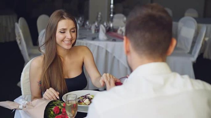 英俊的年轻人向惊讶的女孩求婚，然后在餐厅浪漫约会时将订婚戒指戴在她的手指上，敬酒和碰杯。