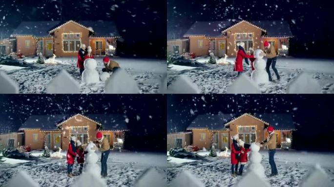 幸福的年轻家庭在他们田园诗般的房子的后院堆雪人。父亲滚雪球，女儿和妻子帮助他。一个冬天的晚上，一家人