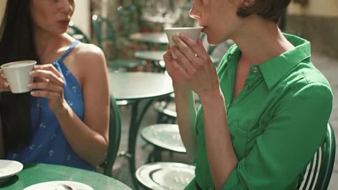 两个穿着轻便夏装的迷人年轻女性在街头咖啡店放松、交谈和喝咖啡。