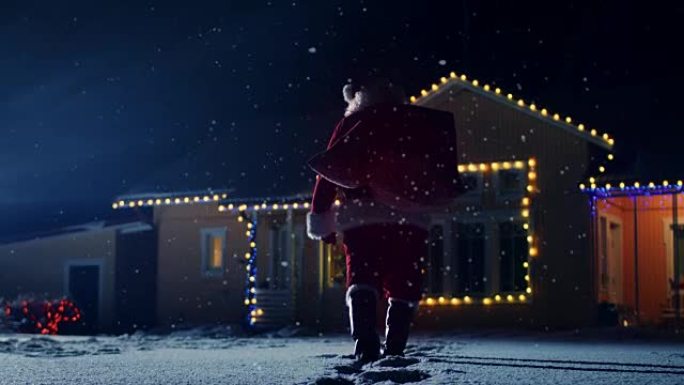 圣诞老人带着红色袋子的低角度镜头，走进装饰着灯光和花环的田园诗般的房子的前院。圣诞老人晚上带礼物和礼