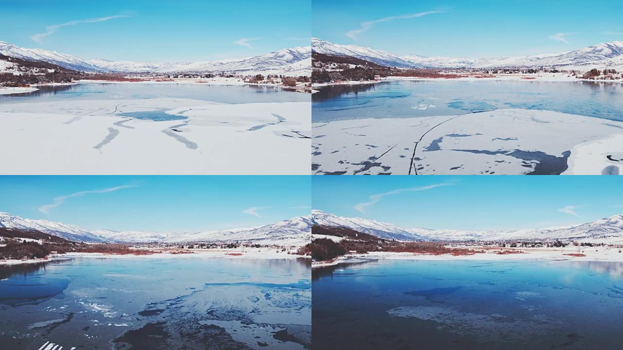 鸟瞰图飞越冬季湖，冰雪覆盖，背景为雪山