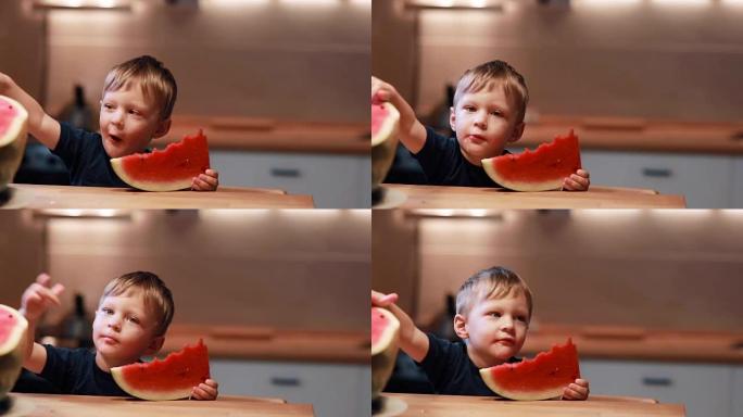 可爱的小男孩坐在厨房的桌子上的肖像。拿着一块，摸着西瓜，舔手指