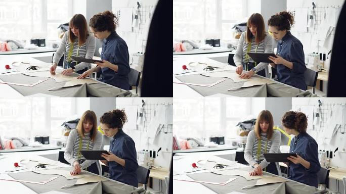 有吸引力的服装设计师企业家正在用粉笔勾勒出剪裁，与平板电脑合作并交谈。成功的裁缝店概念忙碌的一天。