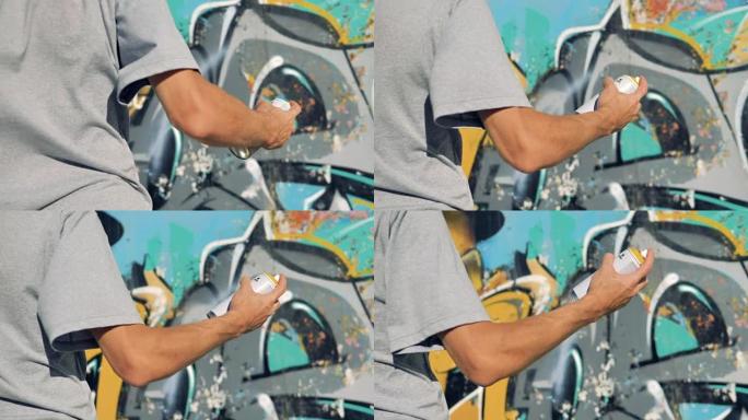 一只手在涂鸦墙附近摇动油漆罐。