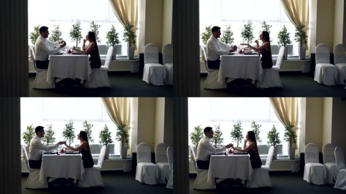 餐馆约会时年轻帅男向漂亮小姐求婚的侧视图。女人感到惊讶和快乐，未婚夫在她的手指上戴上戒指。