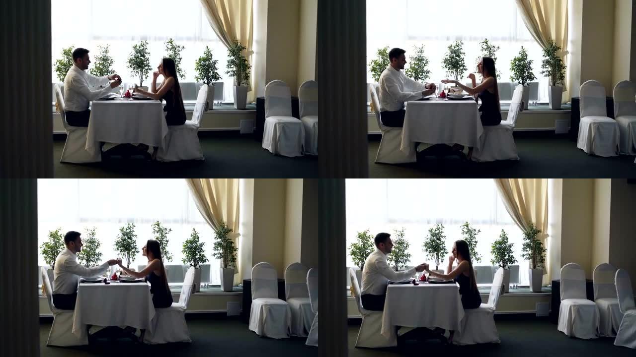 餐馆约会时年轻帅男向漂亮小姐求婚的侧视图。女人感到惊讶和快乐，未婚夫在她的手指上戴上戒指。