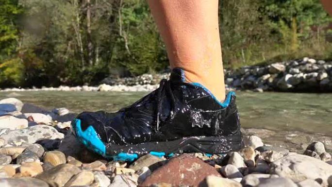 慢动作，特写: 当女人走出河里时，水从运动鞋上溅起。
