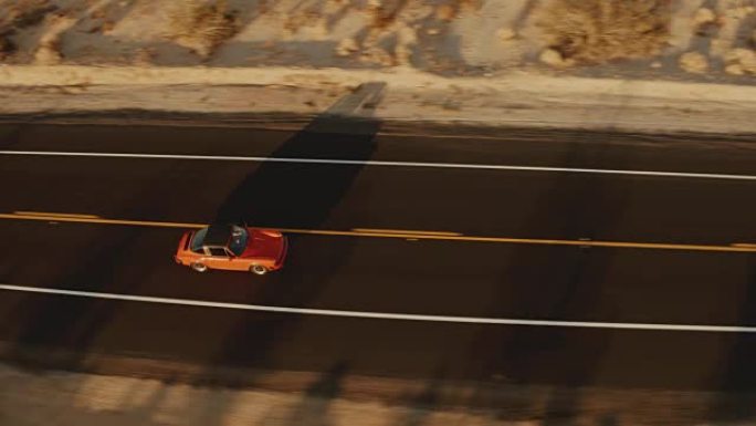 鸟瞰图红色经典汽车在日落时沿着荒凉的沙漠路行驶