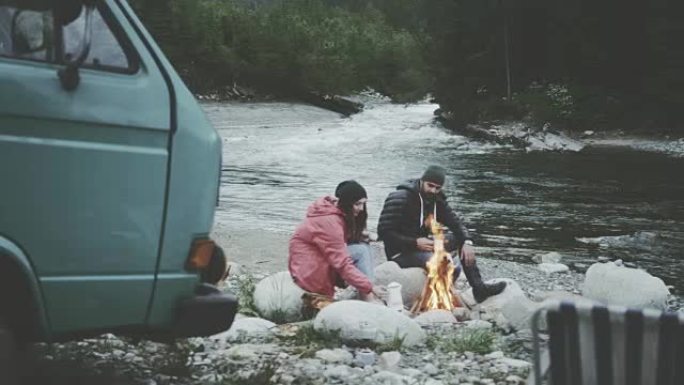 年轻夫妇在炉火旁放松。露营者在后台。山地景观