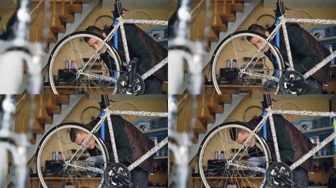 忙碌的服务员正在检查后轮旋转踏板，并在工作室修理自行车时看着辐条。漂亮的车间内部是背景。