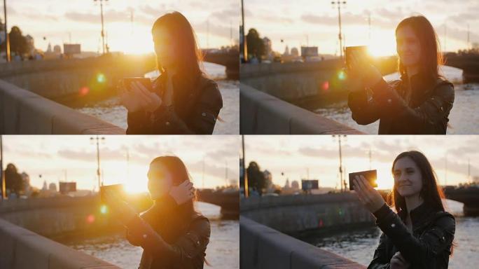 年轻漂亮的女孩在夕阳的明亮光线下在桥的背景上自拍。全高清