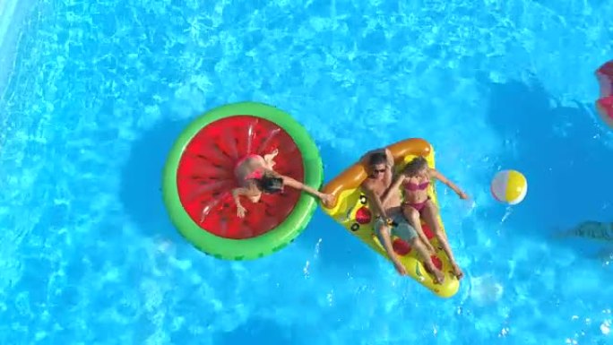空中: 快乐的青少年在泳池水中充气的彩色浮标上玩得开心
