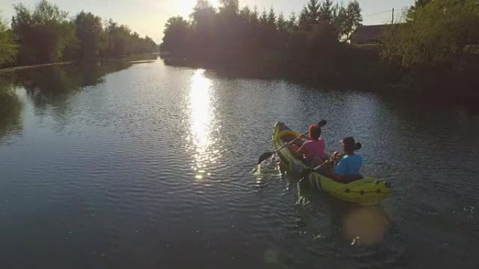 空中: 皮划艇夫妇沿着平静的河流向美丽的夏日日落划船