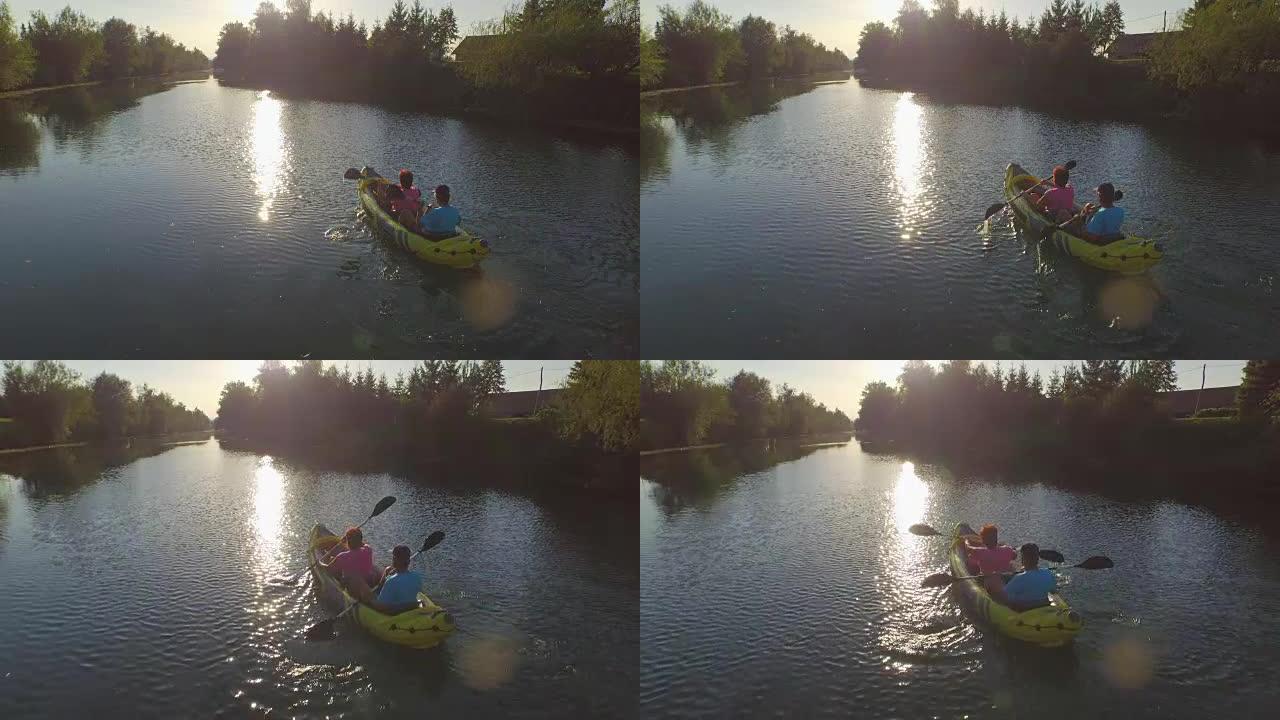 空中: 皮划艇夫妇沿着平静的河流向美丽的夏日日落划船