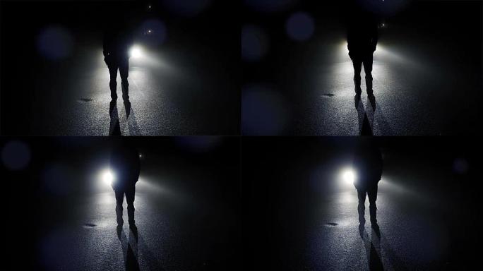 黑暗中站在汽车前的人的轮廓。晚上有阴影和背光。