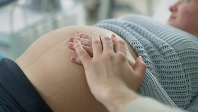 在医院里，特写孕妇的肚子，她和丈夫小心翼翼地触摸它，试图感觉到婴儿是否踢。温柔的家庭时刻。