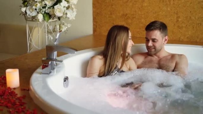 年轻有魅力的人在现代水疗中心的泡沫浴缸里拥抱和交谈。浪漫关系、谈话和健康概念。