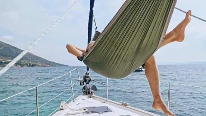 4k男子在吊床上放松，在阳光明媚的帆船上摇摆，实时