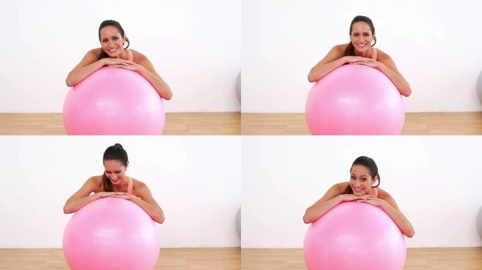 健身模特靠在粉红色的健身球上，对着镜头微笑