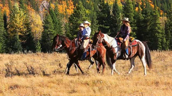 牛仔和两个牛仔女孩骑马穿过山麓