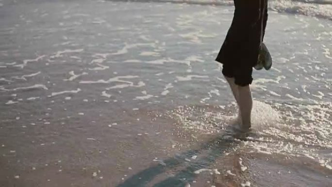 一个年轻人正走在美丽的海滩上，牛仔裤卷起来，把脚浸在海里