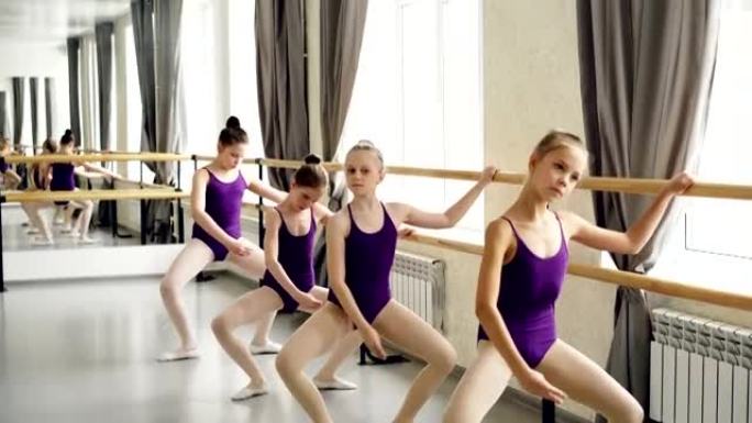 小女孩开始穿着紧身连衣裤的芭蕾舞演员正在拿着芭蕾舞吧练习不同的姿势。舞蹈课，人和室内概念。