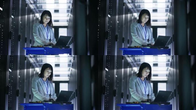 亚洲女IT工程师在一个大型数据中心满是机架服务器的应急手推车笔记本上工作。