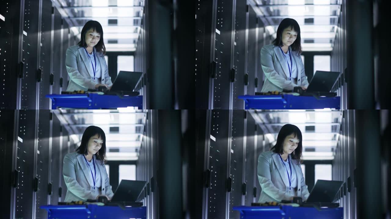 亚洲女IT工程师在一个大型数据中心满是机架服务器的应急手推车笔记本上工作。