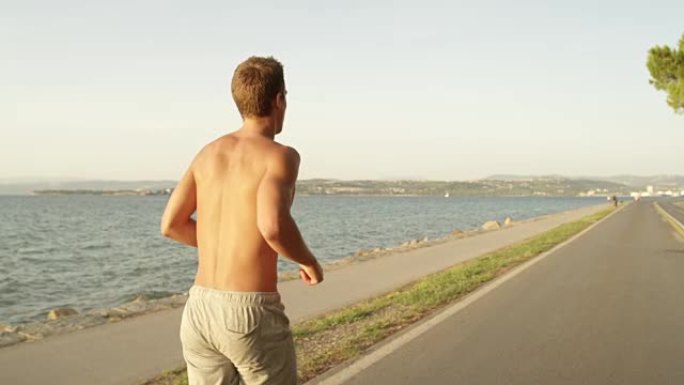慢动作: 面目全非的晒黑男性光着膀子沿着空旷的海洋道路奔跑。