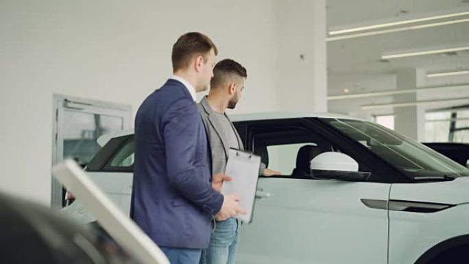 严肃的人正在汽车陈列室与汽车经销商交谈，讨论新的汽车模型，salesmanis拿着文件。购买车辆和人