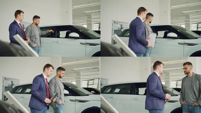 严肃的人正在汽车陈列室与汽车经销商交谈，讨论新的汽车模型，salesmanis拿着文件。购买车辆和人