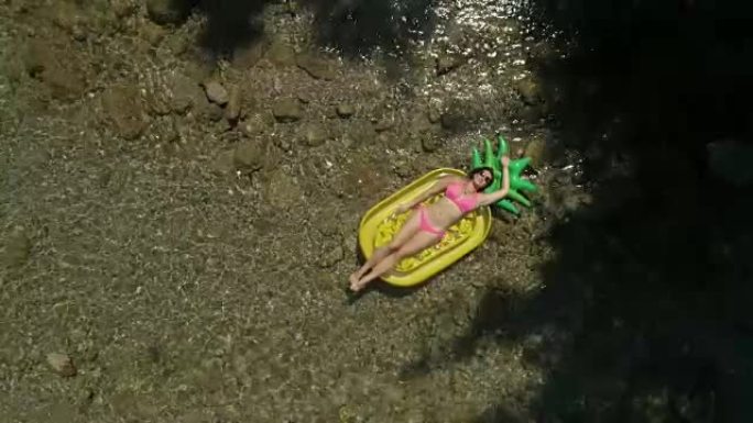 空中: 美丽的女人在菠萝漂浮物上享受暑假。