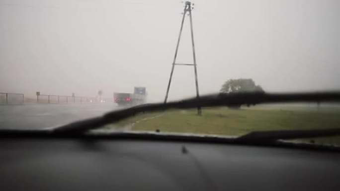 雨刮器在雨中工作在挡风玻璃上。有汽车的道路视图