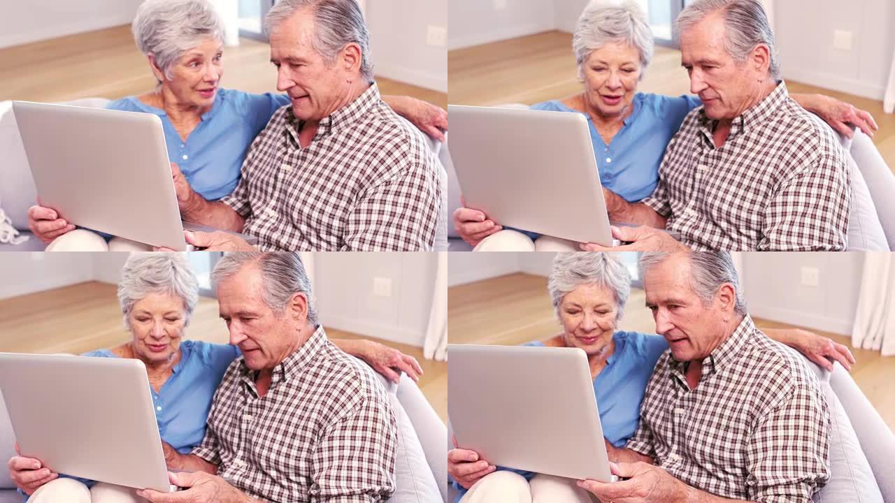 可爱的成熟夫妇在沙发上使用笔记本电脑