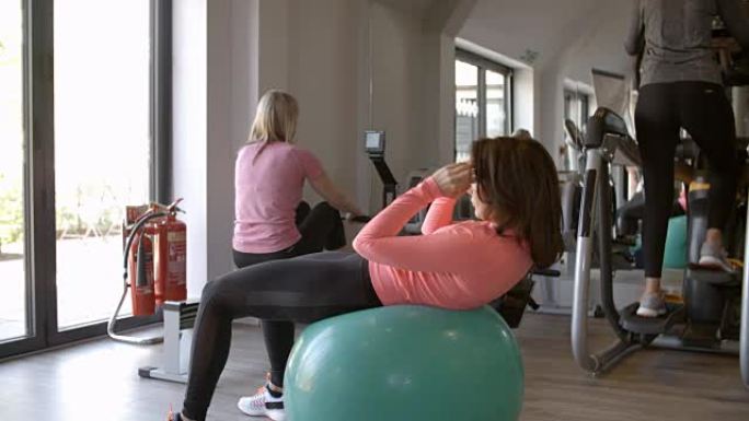 女人在健身房的健身球上做嘎吱嘎吱的事，侧视图