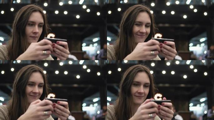 特写肖像。女人在背景4k的现代咖啡厅灯光中使用她的smartphon触摸屏设备