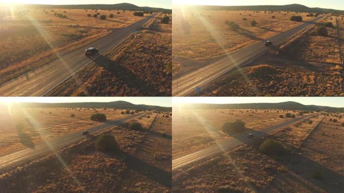 空中: 黑色SUV汽车在金色的夏日日落时沿着空旷的乡间小路行驶