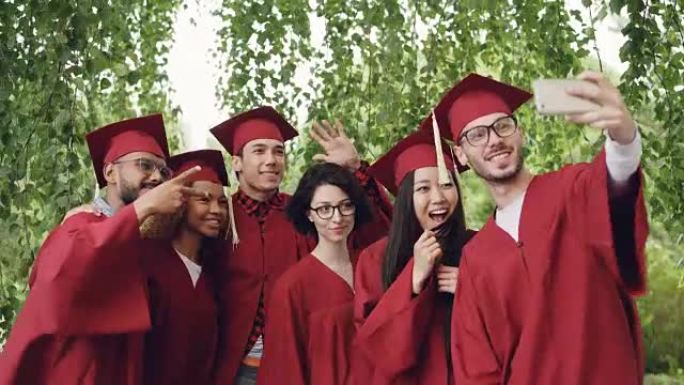 欢快的朋友即将毕业的学生正在用智能手机自拍，年轻人正在摆姿势，展示手势，做鬼脸和大笑。