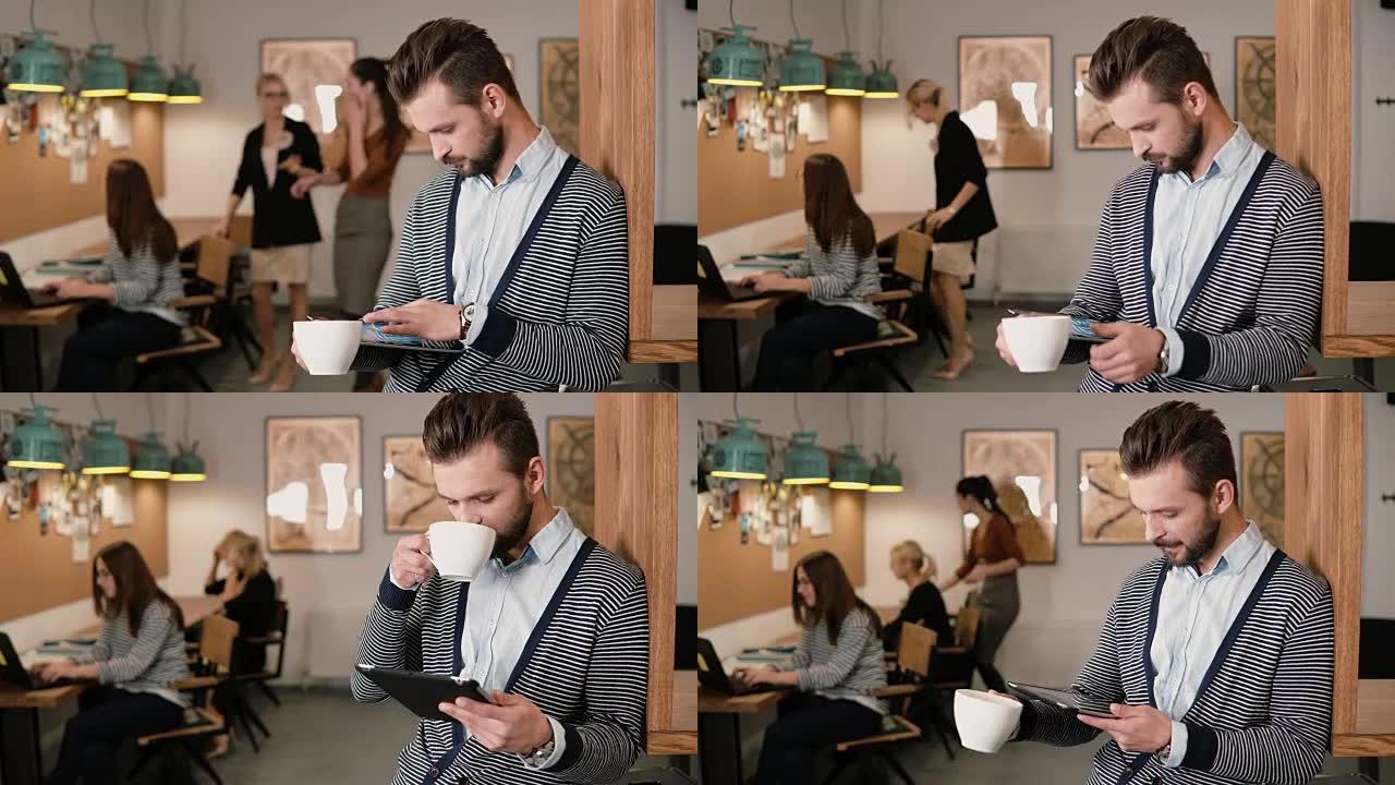 年轻英俊的大胡子男人在现代创业办公室使用触摸屏平板电脑和喝咖啡