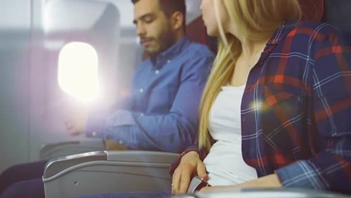 在飞机上，美丽的金发女性和英俊的西班牙裔男性系好安全带，准备起飞/降落。阳光透过飞机的窗户。