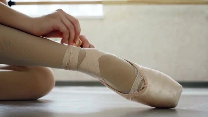 小女孩的脚踩足尖鞋的特写镜头，双手穿上专业的鞋子，并在腿上系丝带。芭蕾舞鞋、舞蹈和服装概念。