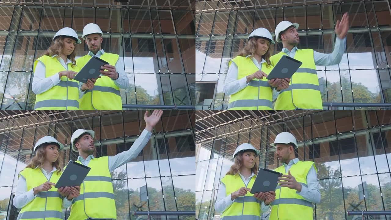 男女工程师在建筑工地进行交谈和使用平板电脑。背景玻璃建筑。